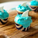 Celebrate Shark Week in the best way possible, with Shark Cupcakes! Moist vanilla cupcakes filled with strawberry jam and topped with the creamiest frosting. Decorated with a shark fin.
