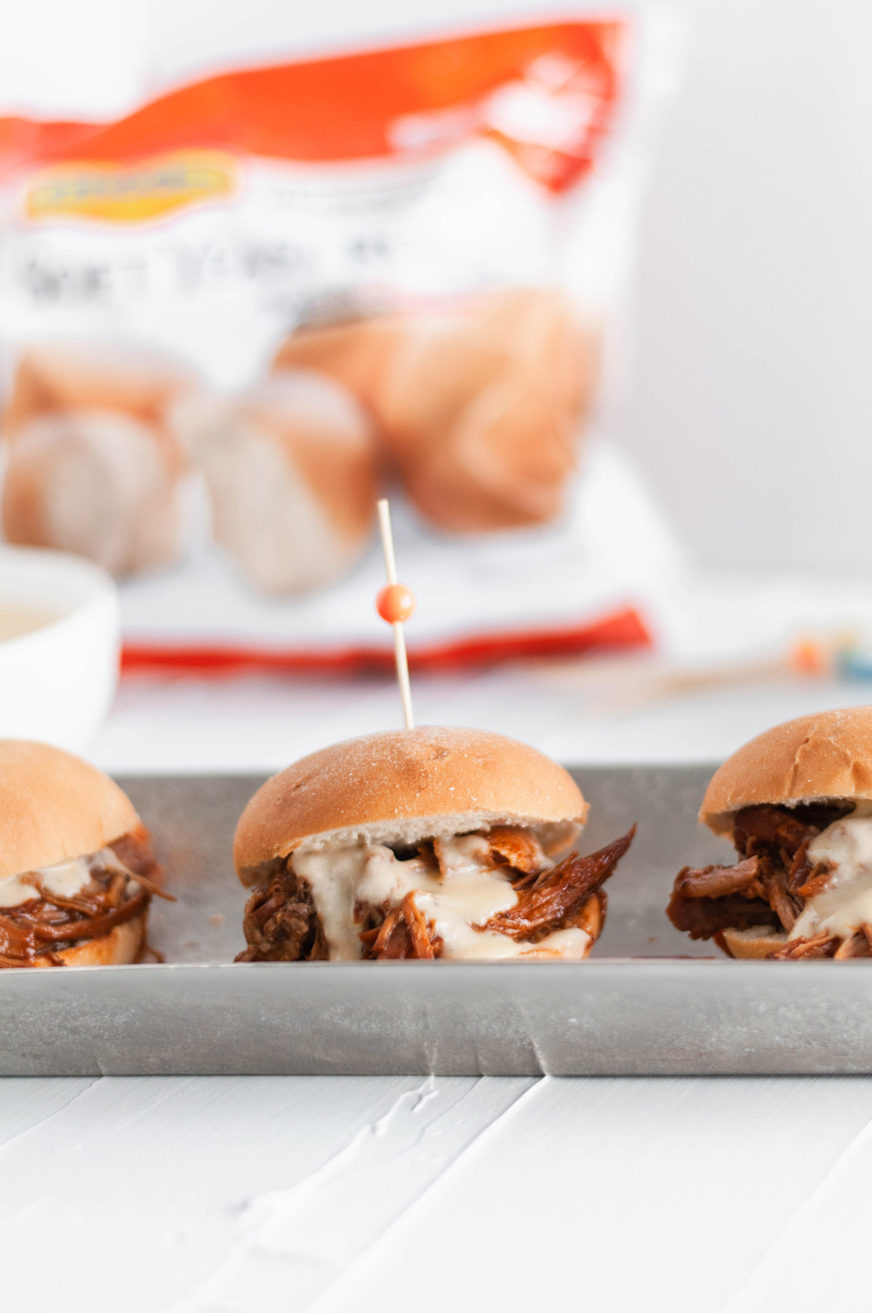 It's football season and that means we need all the delicious party food. Start the game off right with these Cheesy Pulled Pork Sliders. Slow cooker pulled pork, barbecue sauce and a rich, cheesy sauce all loaded atop a soft, pillowy Rhodes Warm-N-Serv roll.