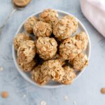 White bowl filled with no bake peanut butter balls. Spoon of peanut butter in background.