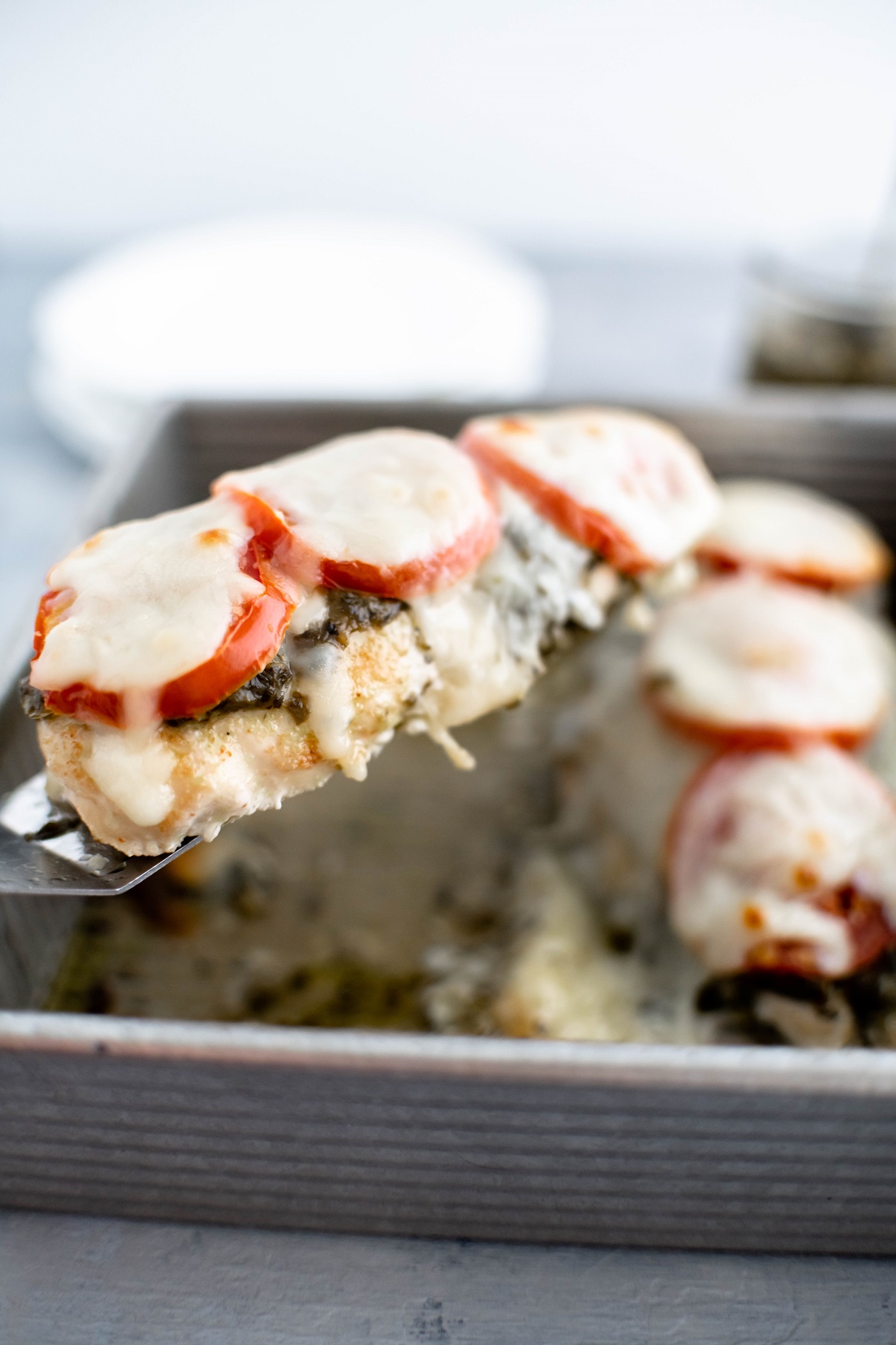 Baked pesto chicken being lifted from baking dish on a small spatula.