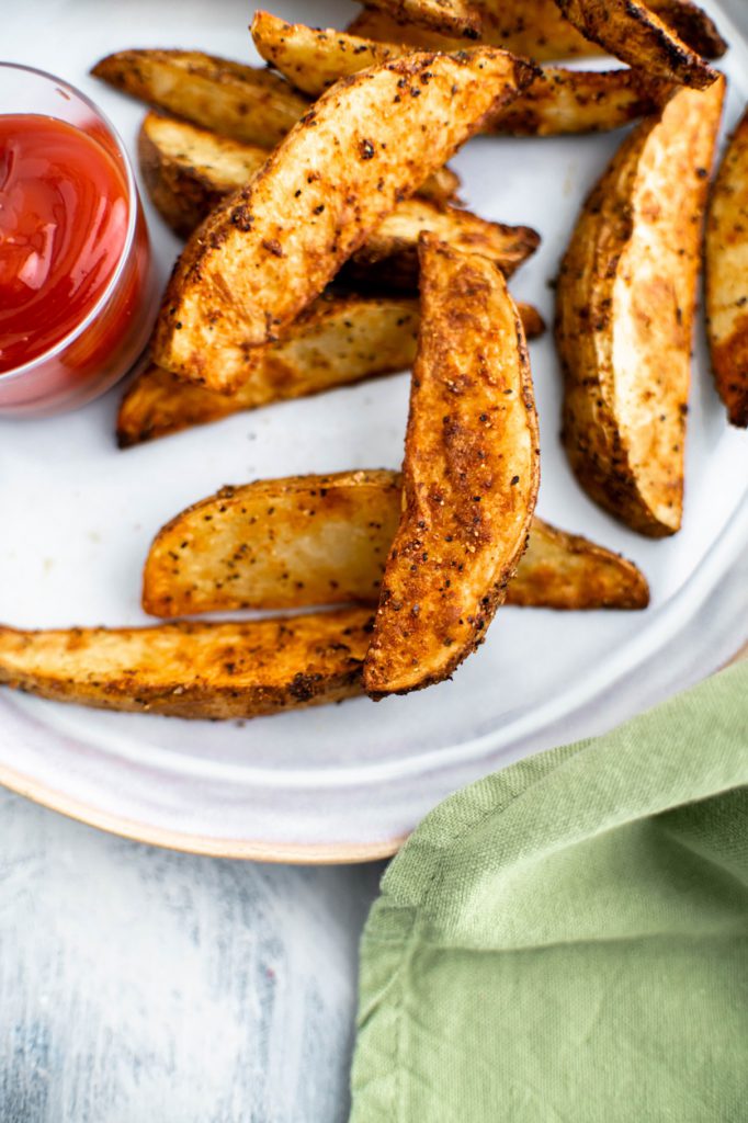 Air fryer potato wedges on a gray plate with a small glass bowl of ketchup on the left side of the plate.