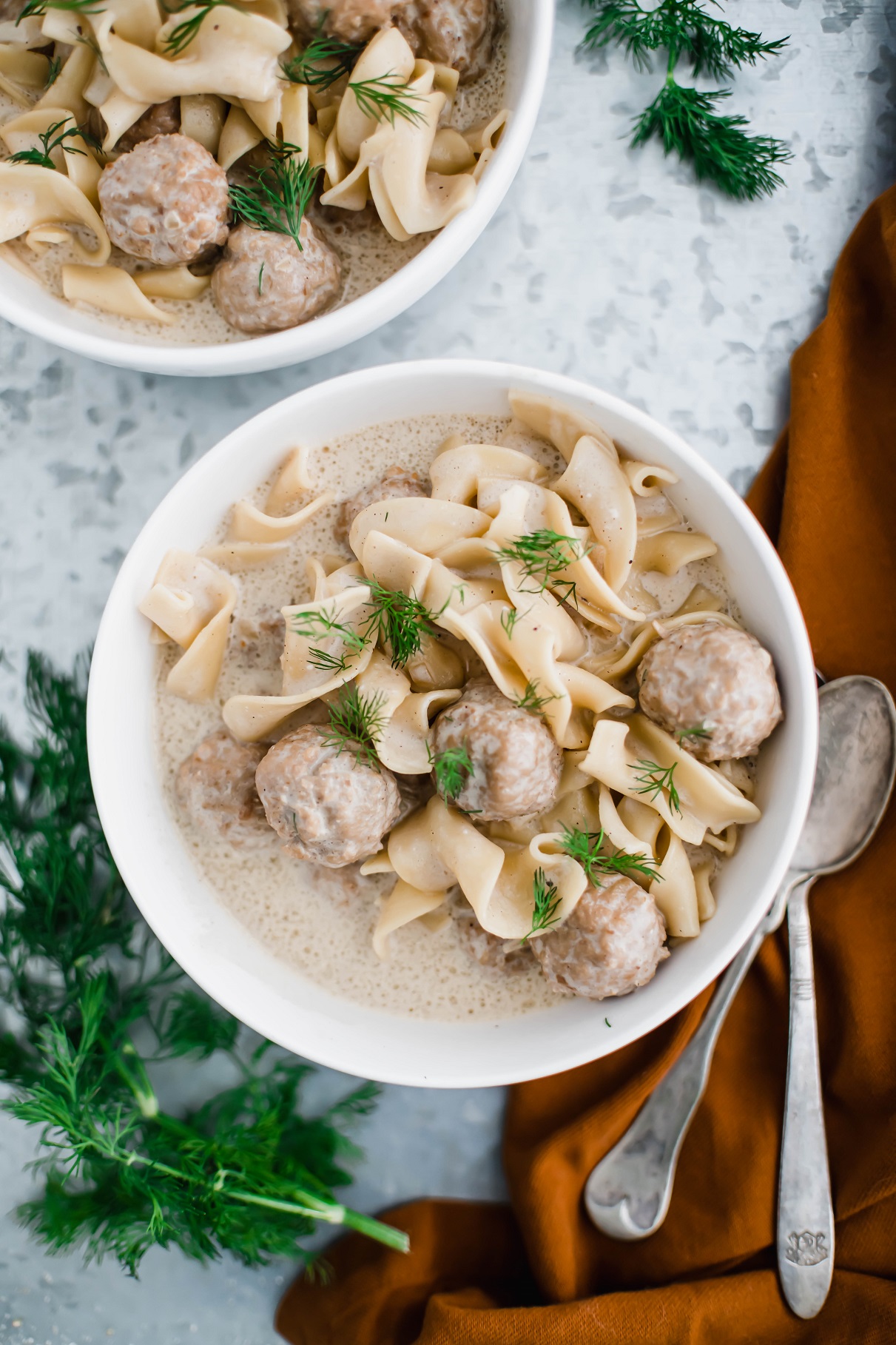 Two bowls of swedish meatball soup garnished with fresh dill. Two spoons to the right side.
