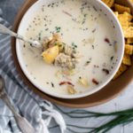 Bowl of clam chowder with spoon lifting out soup to see texture.