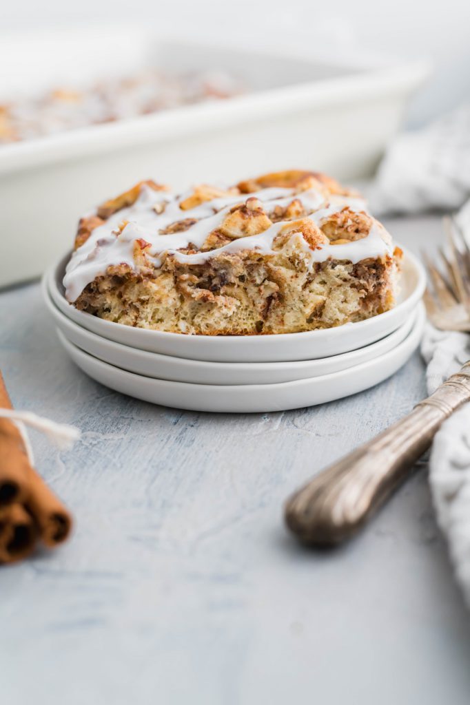 Slice of cinnamon roll casserole on a small white plate with casserole dish in the background.