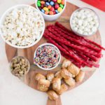 Wooden board filled with soft pretzels, candy, popcorn and nights for a movie night snack board.