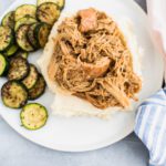 Round white plate with shredded honey mustard chicken on top of mashed potatoes with a side of sauteed zucchini.