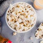 Bowl of Instant Pot Popcorn with a metal scoop of popcorn to the side and shaker of salt.