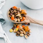 Wooden ladle filled and overflowing with peanut butter trail mix with a white bowl of trail mix in the background.