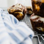 Chocolate cream cheese muffins stacked in a pile in the forefront of the photo another in the background that is the focus.