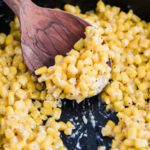 Honey butter corn in a cast iron skillet with a wooden spoon scooping out some.
