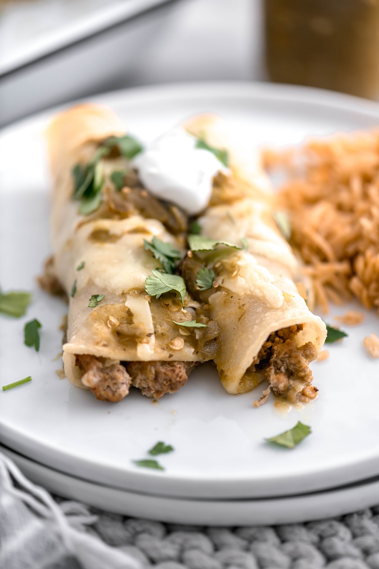 Two turkey enchiladas on a round white plate with a side of Mexican rice.