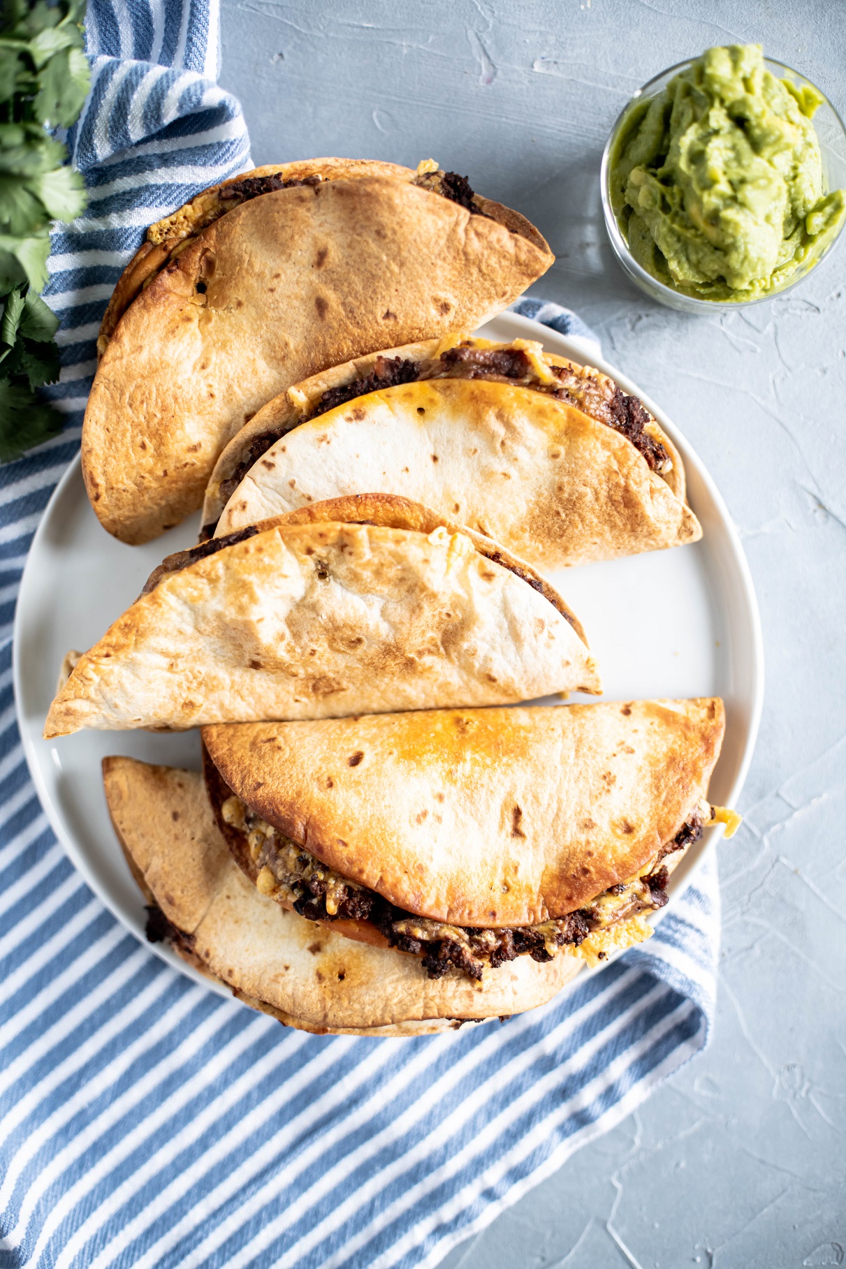 4 tacos on a round white plate.