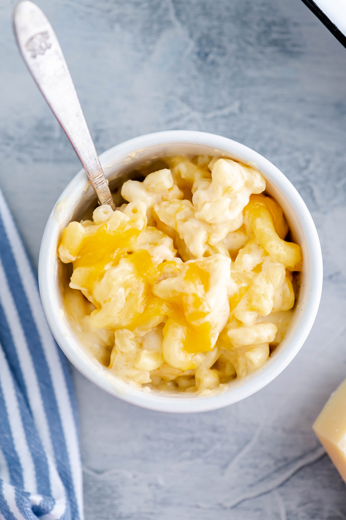 White bowl filled with macaroni and cheese with blue and white striped napkin to the left.