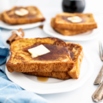 Three small white plates, each with two pieces of spiced french toast topped with butter and maple syrup.