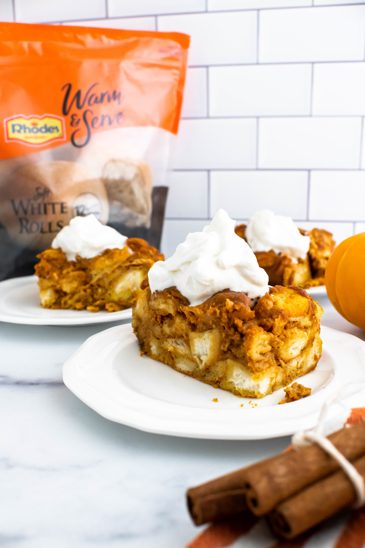 Three plates each with a portion of pumpkin bread pudding topped with fresh whipped cream.