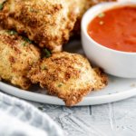 White round plate filled with air fryer ravioli and a small white round bowl filled with marinara sauce.