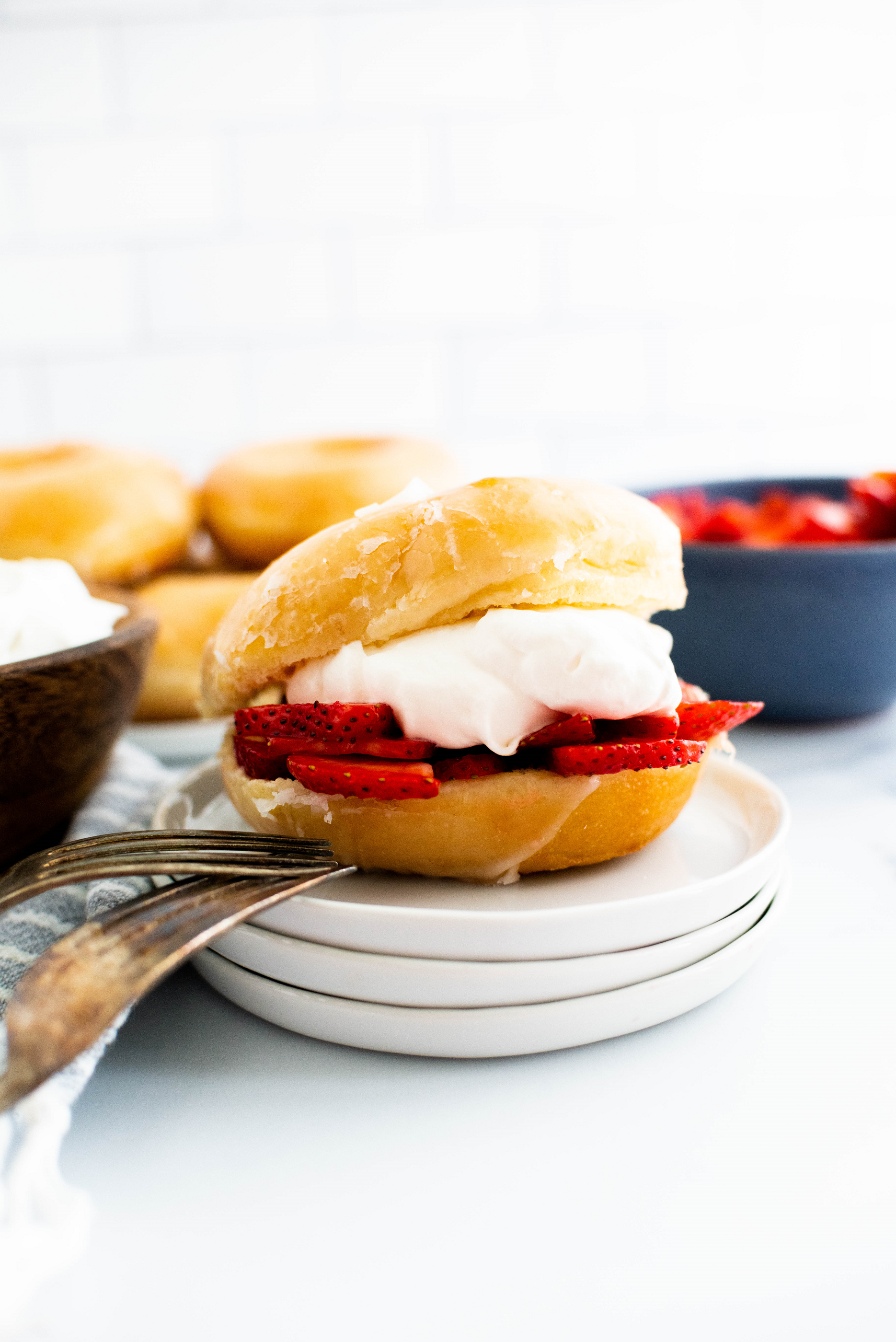 Glazed donut filled with macerated strawberries and fresh whipped cream on a small white plate.