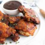 Air fryer bbq chicken on a round white plate with a small white bowl filled with barbecue sauce.