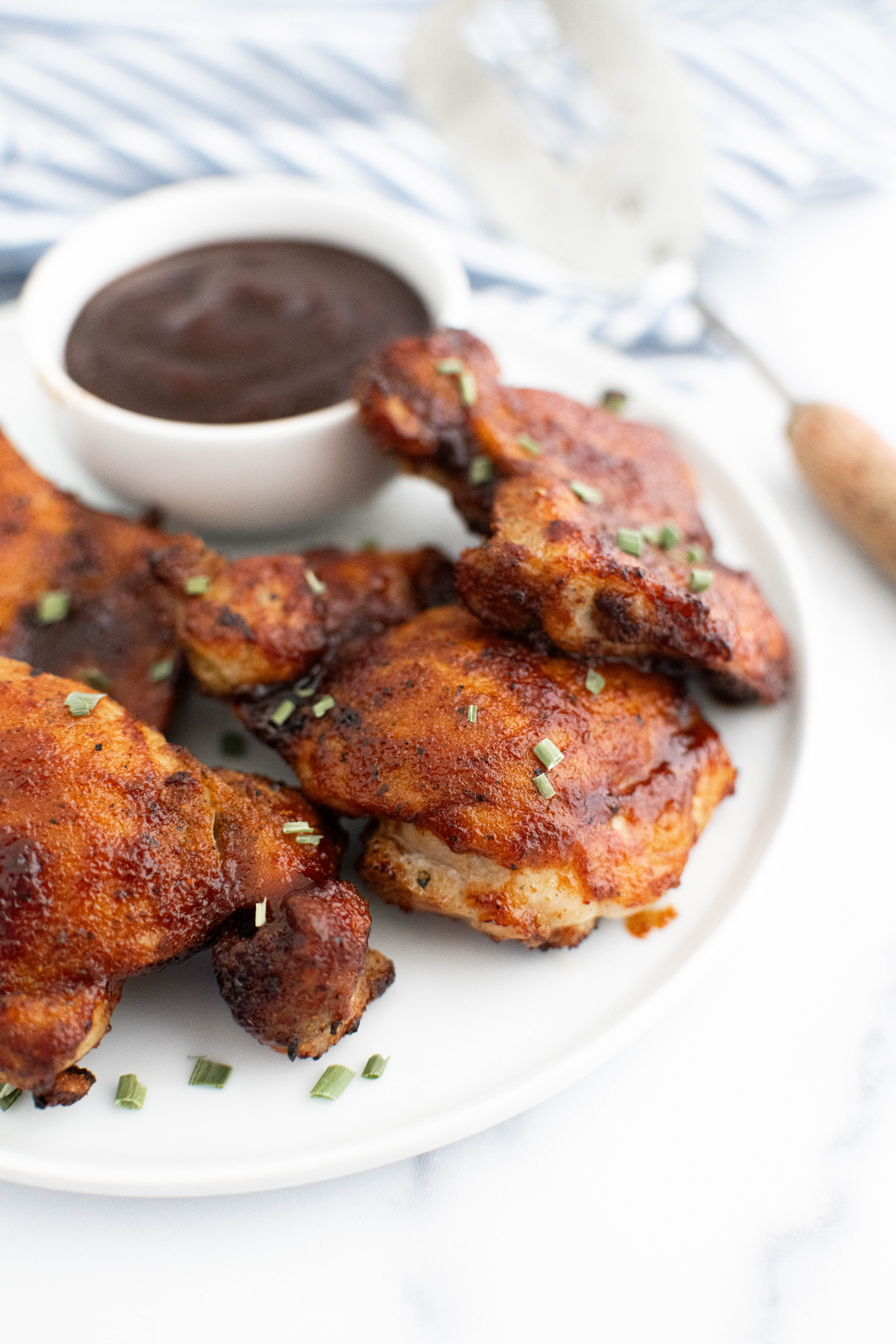 Air fryer bbq chicken on a round white plate with a small white bowl filled with barbecue sauce.